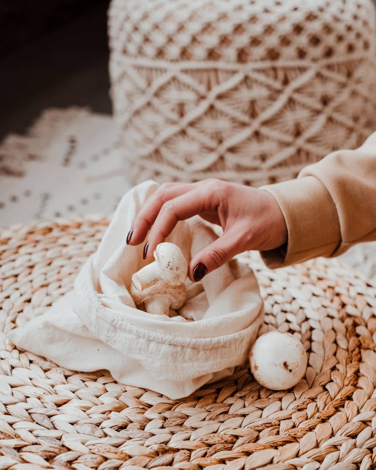 A cloth mushroom bag on a woven placemat with a hand taking mushrooms out of the bag. 