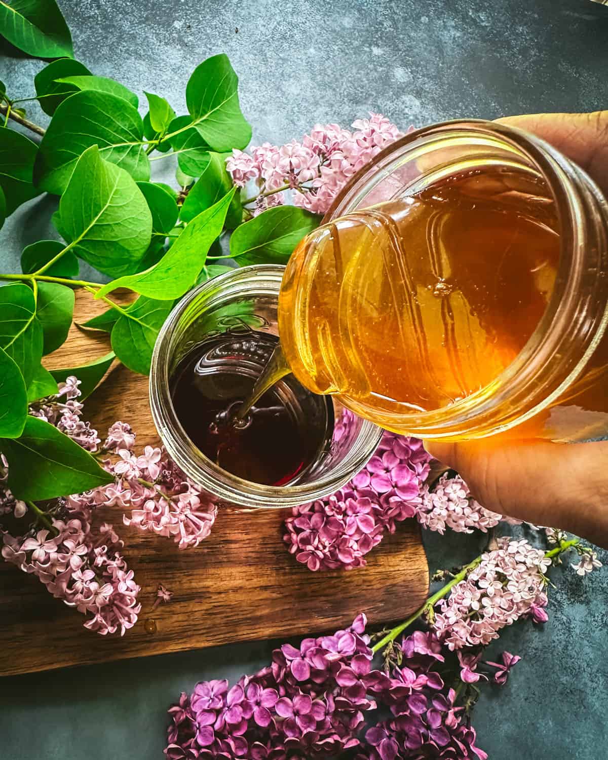 Honey pouring into the lilac tea, surrounded by fresh lilac flowers. 