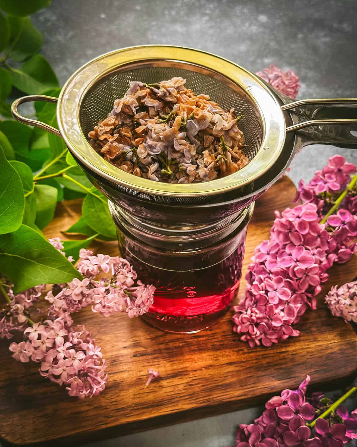 A jar of lilacs being strained from tea into a mesh strainer. 
