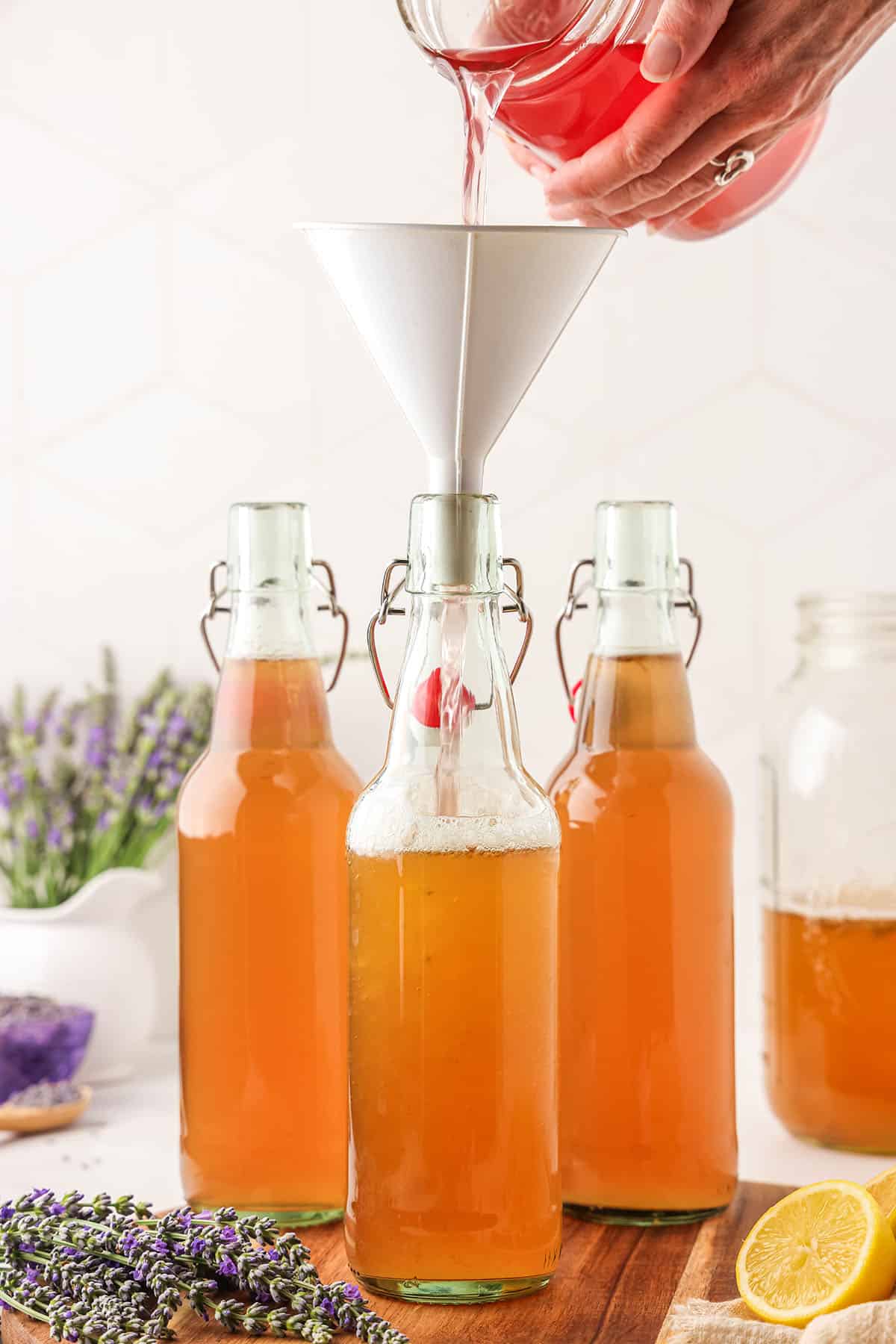 Lavender syrup pouring into flip top bottles half filled with kombucha.