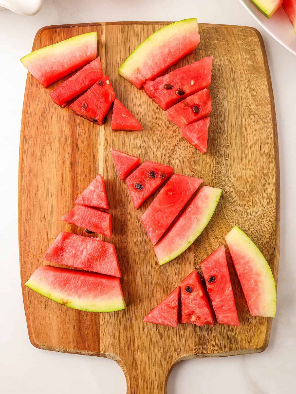 Triangles of sliced watermelon cut into small pieces on a wooden cutting board. 