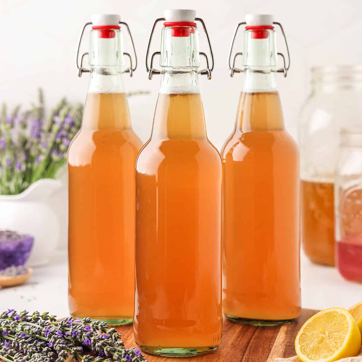 3 flip top bottles of lavender kombucha, surrounded by fresh lemon and lavender.
