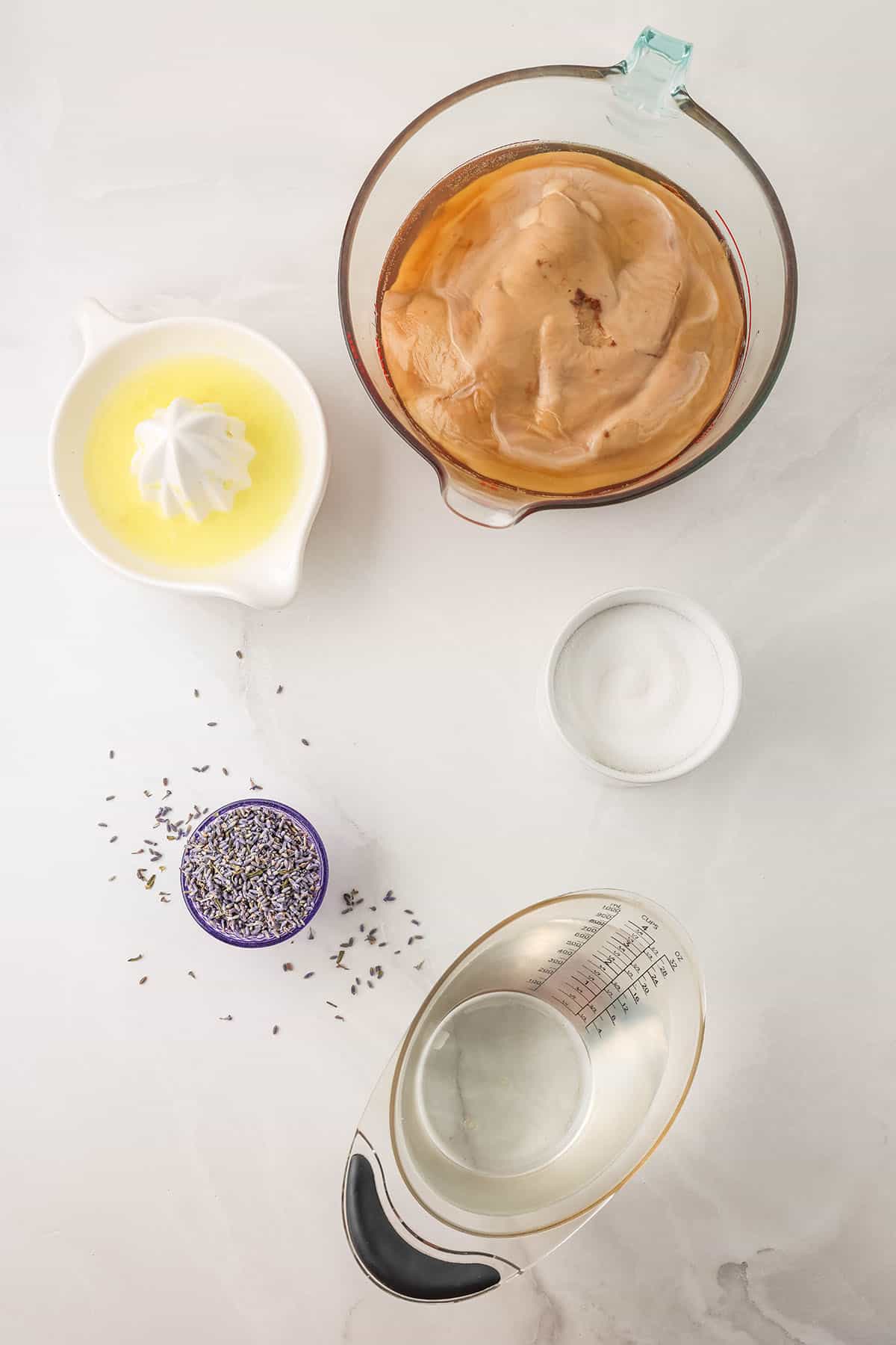 Lavender kombucha ingredients in bowls on a white countertop, top view.