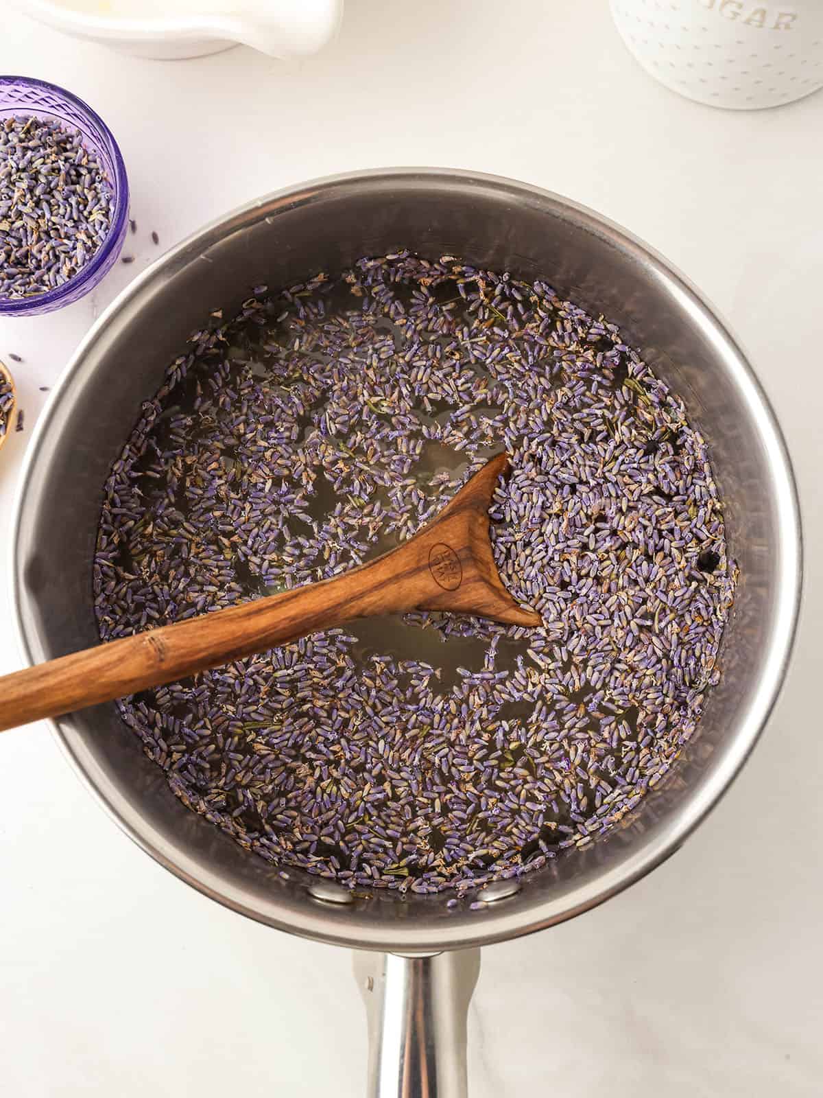 A pot of lavender tea with a wooden spoon in it, top view on a white countertop.