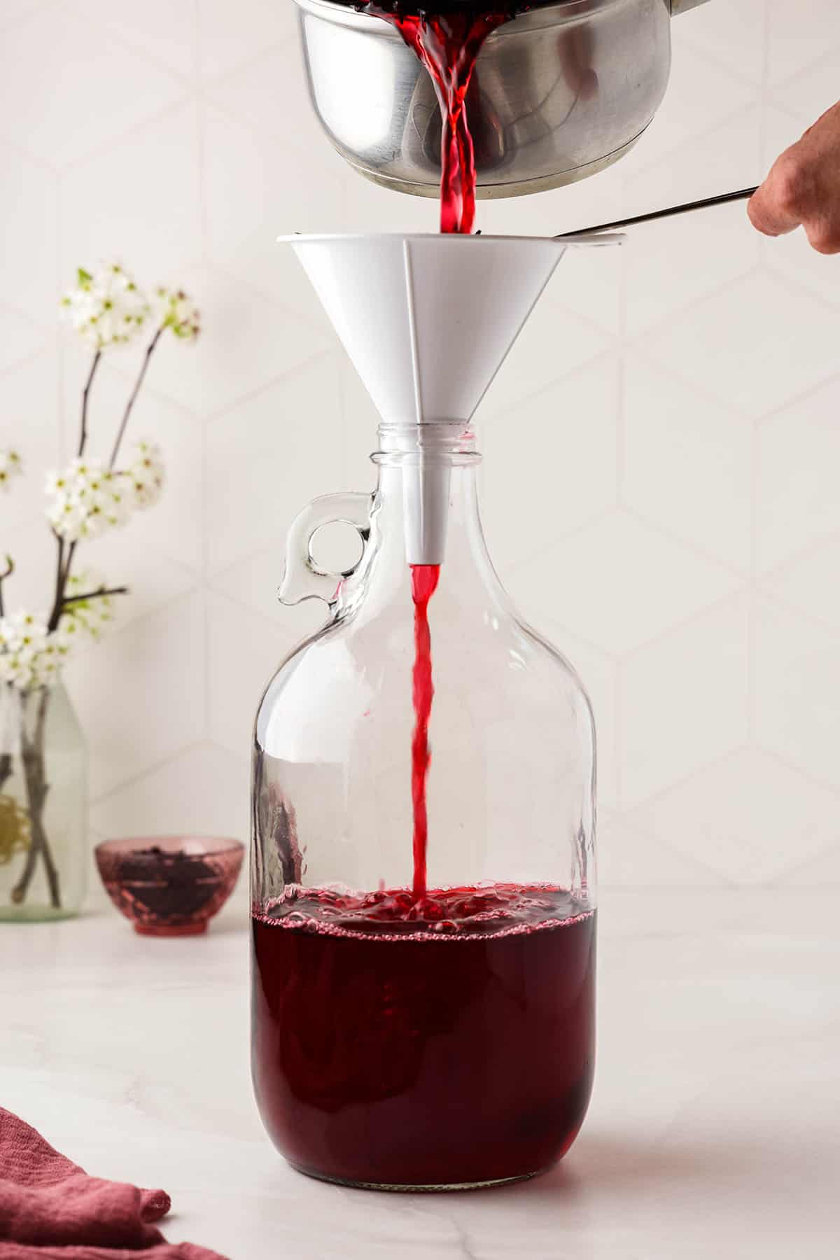 Hibiscus tea straining through a funnel into a bottle, on a white surface. 