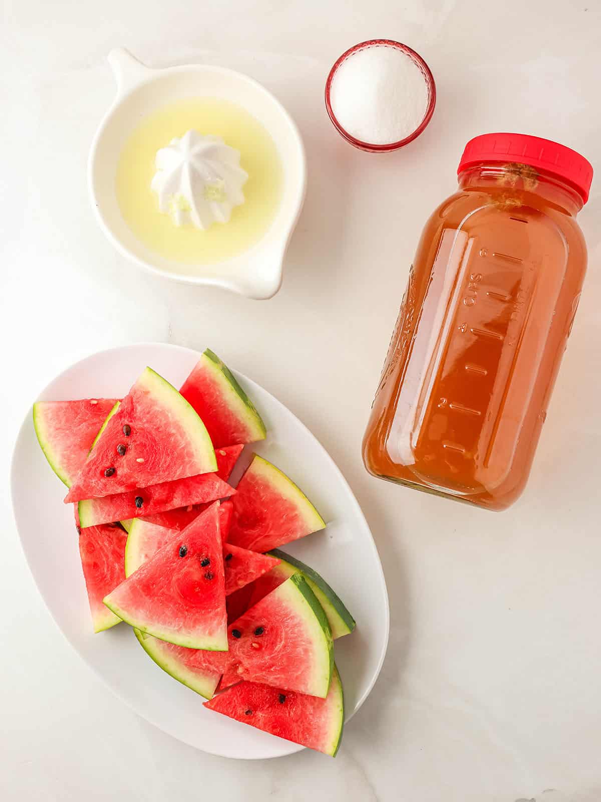 Ingredients for watermelon kombucha on a white countertop, top view. 