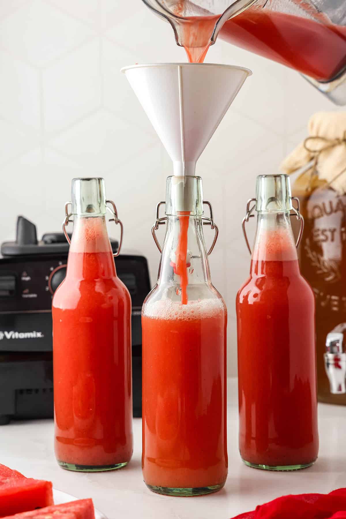 Swing top bottles with watermelon puree being added to the kombucha to fill with a funnel on top. 