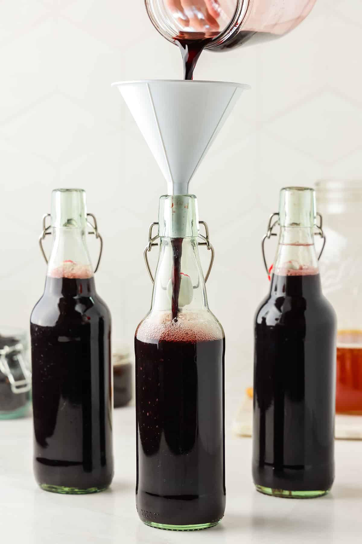 Bottles of kombucha being filled with elderberry syrup, with a little bit of space left at the top. 