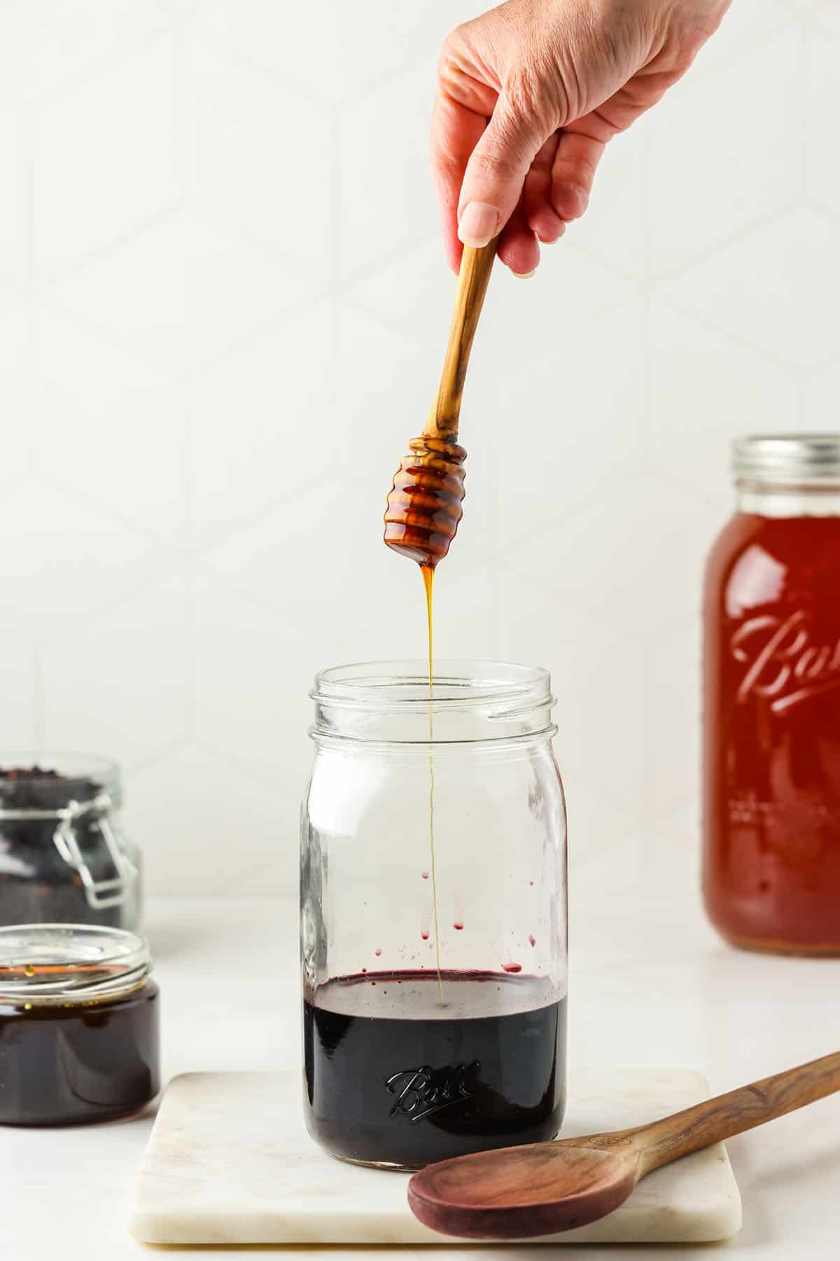 Honey is added to a jar of elderberry tea with a honey stick. 