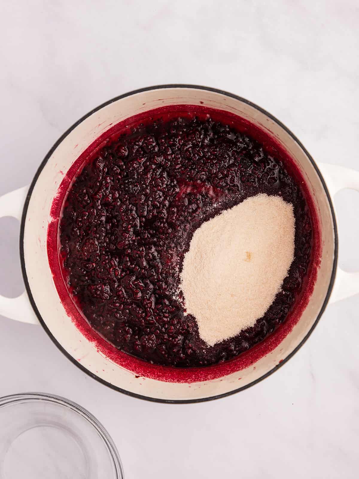 Blackberry mash in a pot with sugar in it ready to be mixed in. 