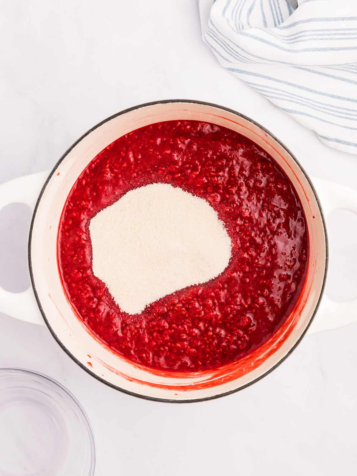 A bowl of mashed raspberries with sugar poured in but not mixed yet, top view. 