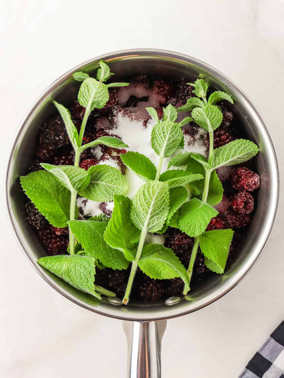 A pot with blackberries, sugar, and fresh mint, top view. 