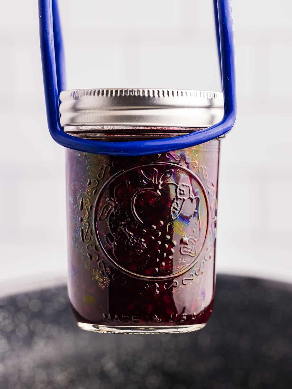 A jar lifter with a jar of blackberry jam lifting out of a water bath canner. 