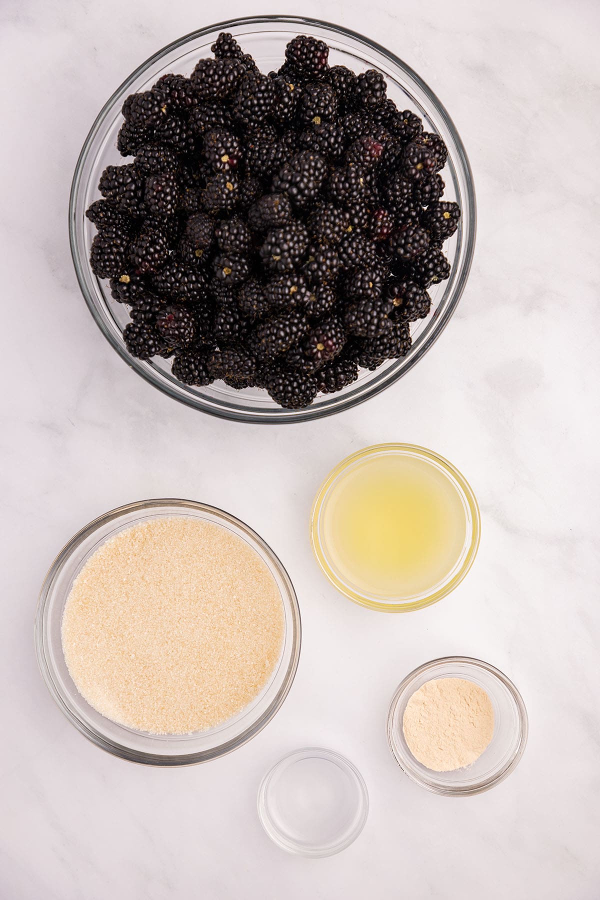 Blackberry jam ingredients in bowls on a white counter, top view. 