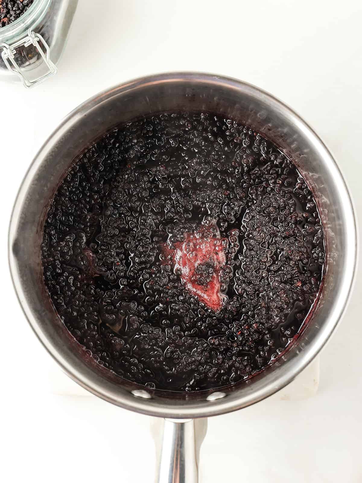 A pot of boiling elderberries on a white counter, top view. 