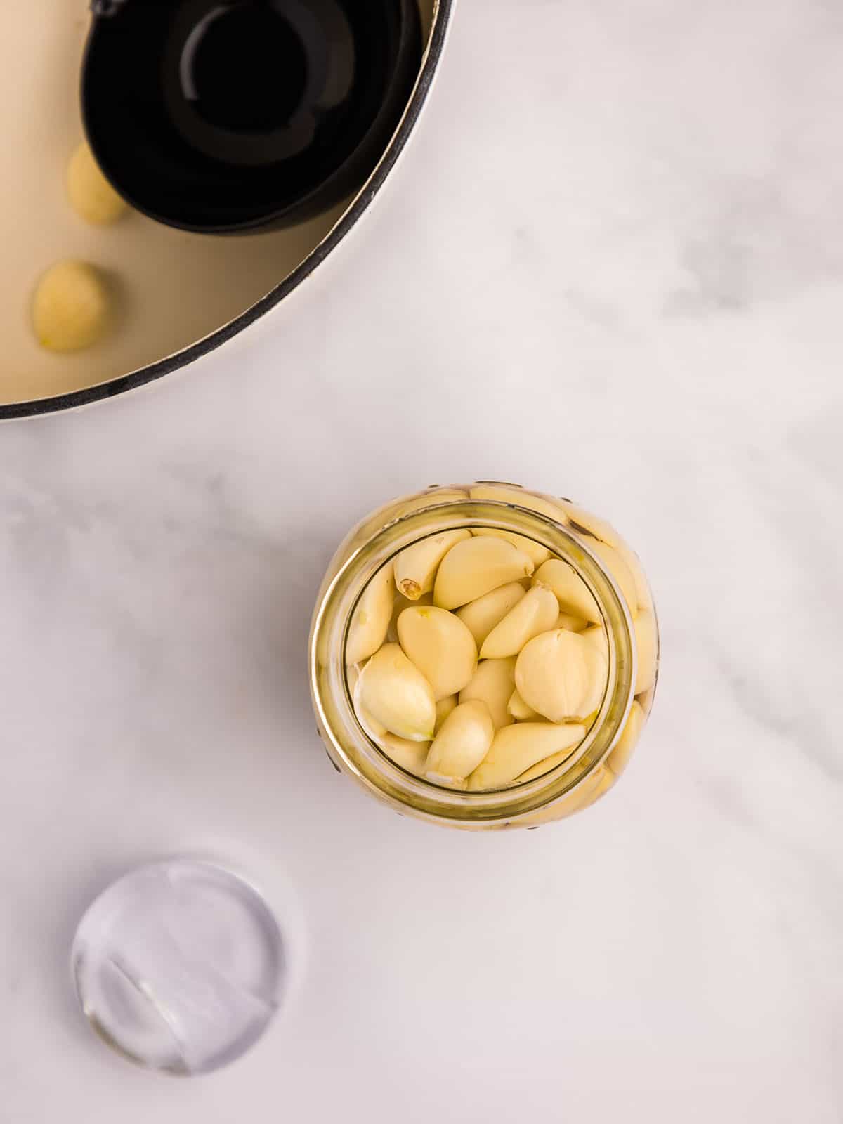 A jar full of garlic, surrounded by other ingredients, top view. 