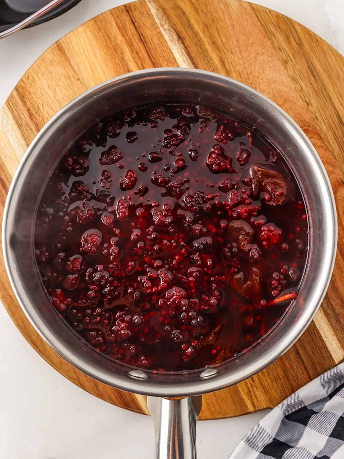 Cooked blackberries in a pot, cooling on a wood surface, top view. 