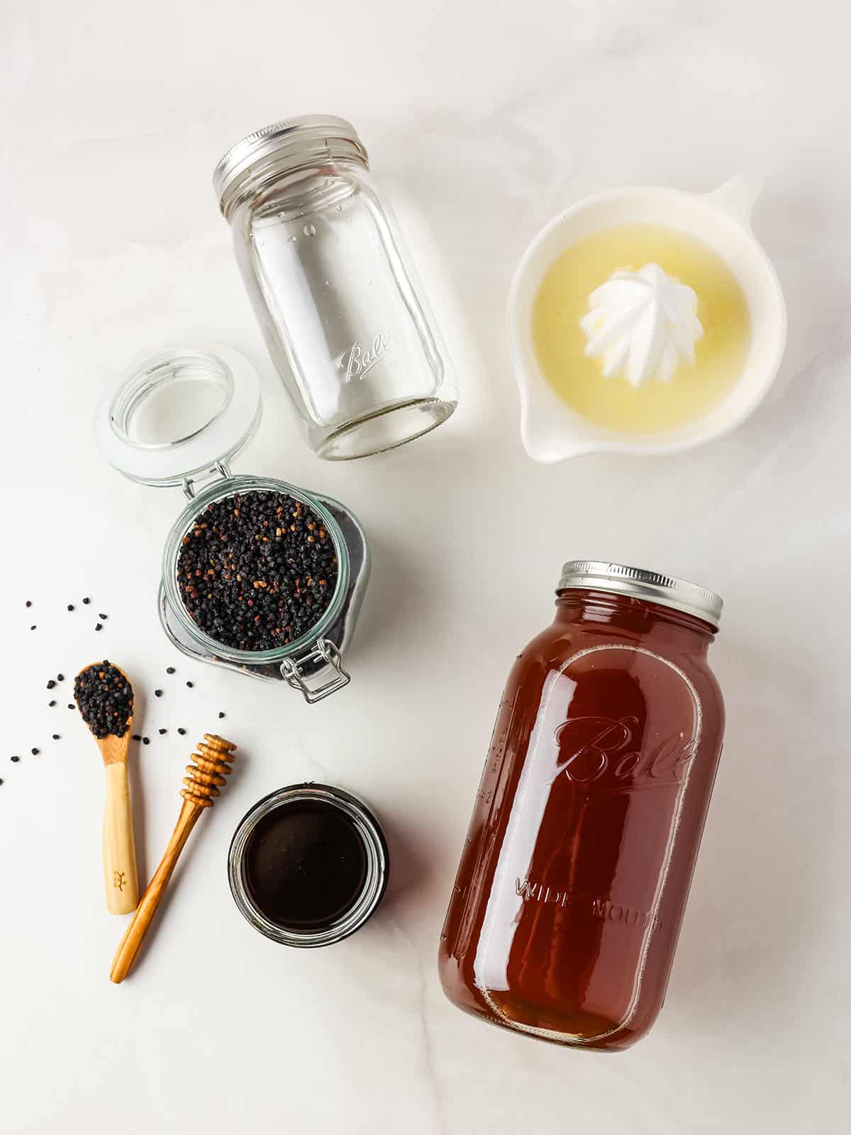 Elderberry kombucha ingredients in dishes on a white counter, top view. 