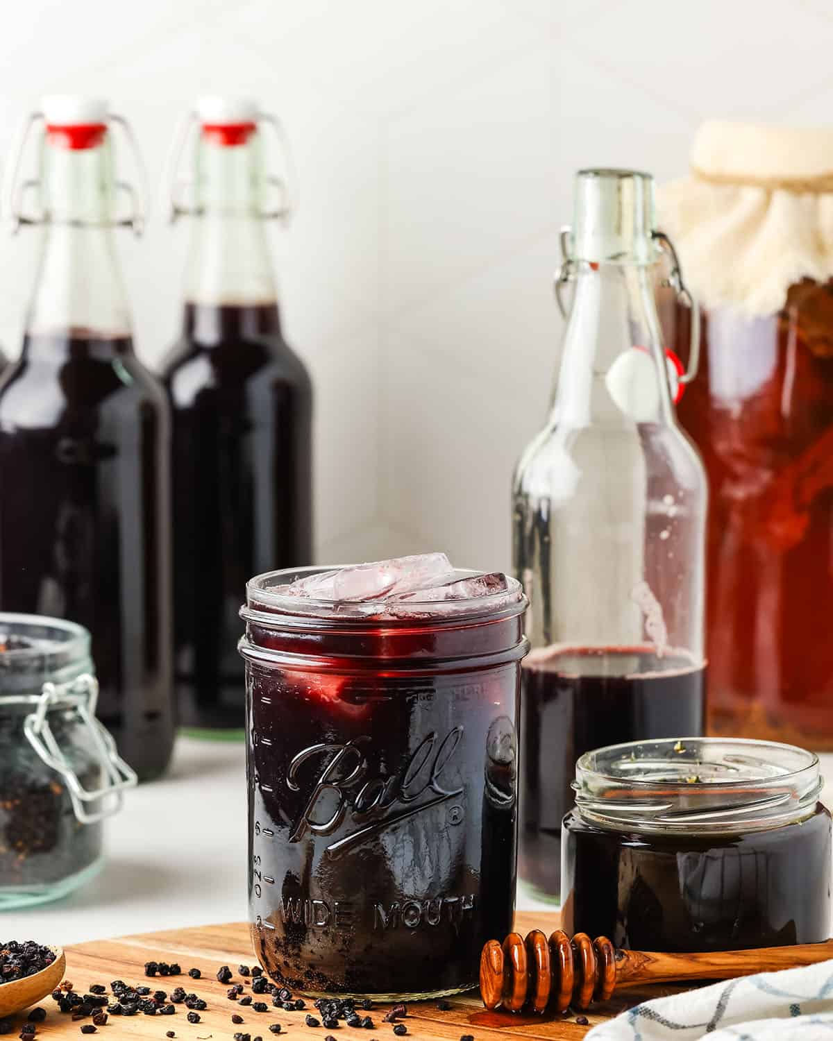 A glass jar of elderberry kombucha on a wood cutting board with other bottles in the background. 