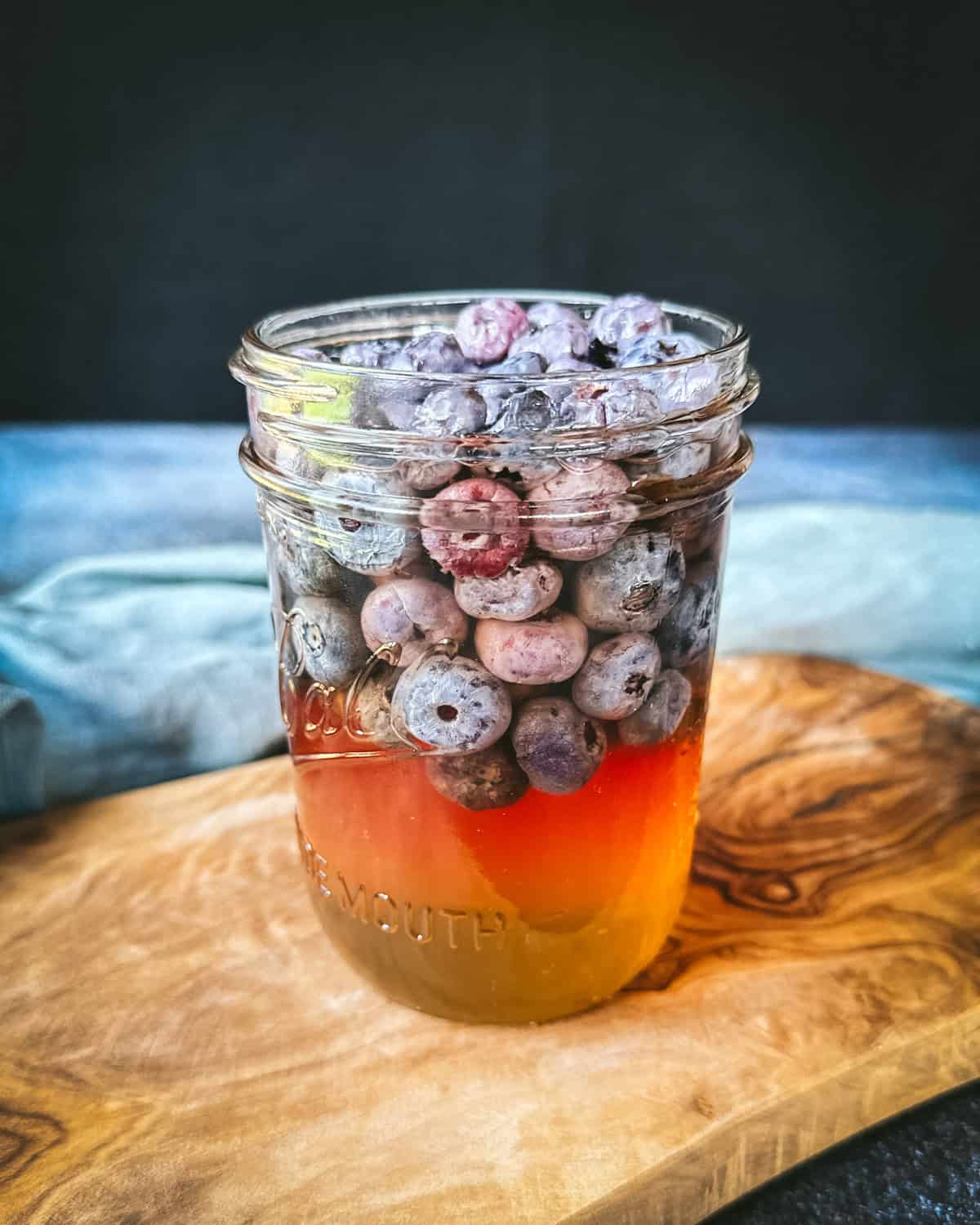 Fermented blueberries in a jar on a wood surface. 