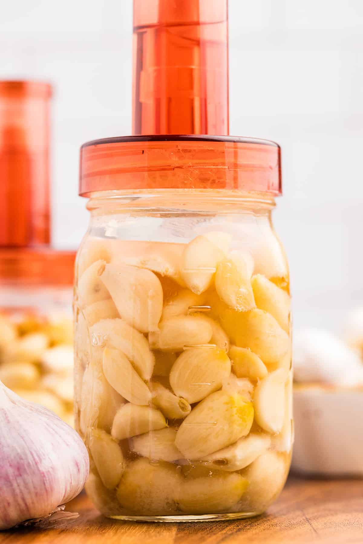 Garlic fermenting in a jar with an orange airlock on top.