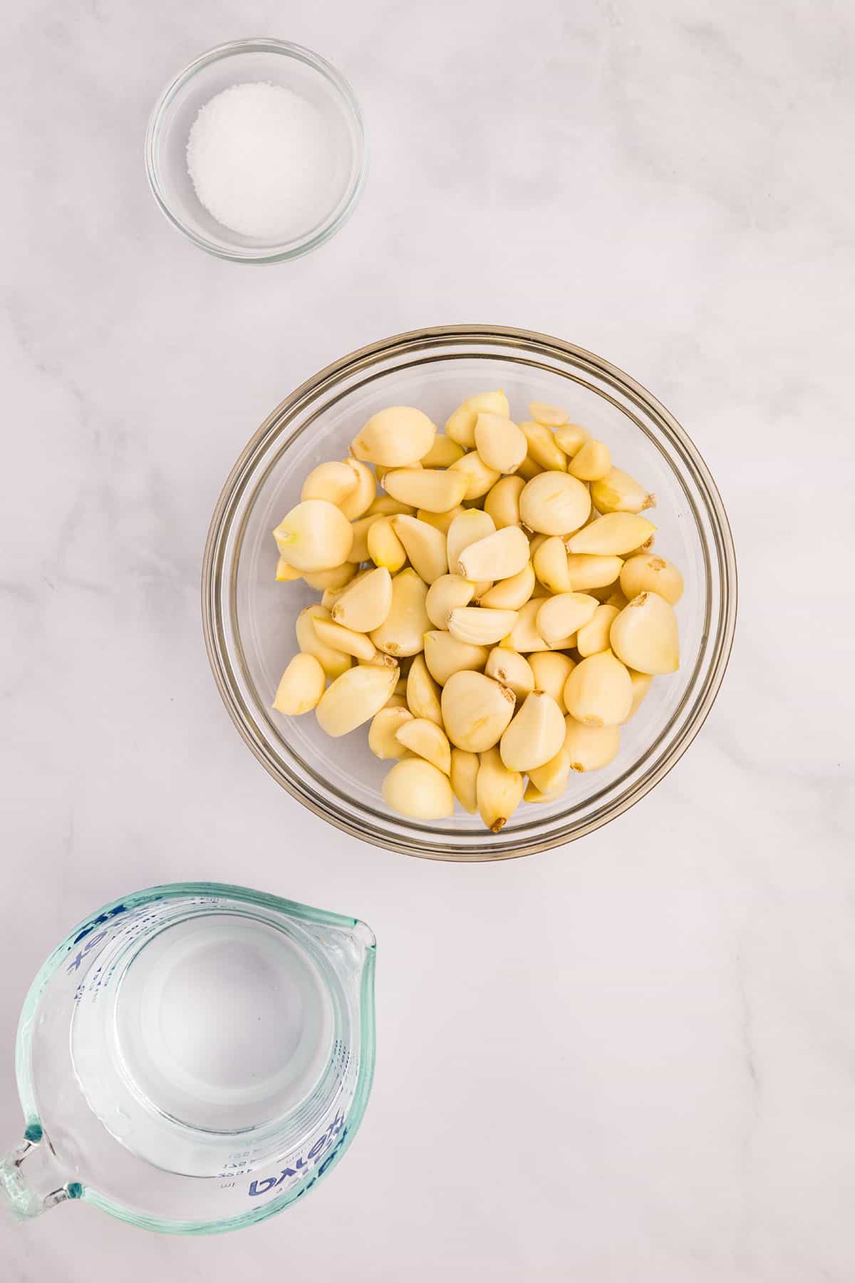 Fermented garlic ingredients in bowls on a counter surface, water, garlic cloves, and salt. Top view. 