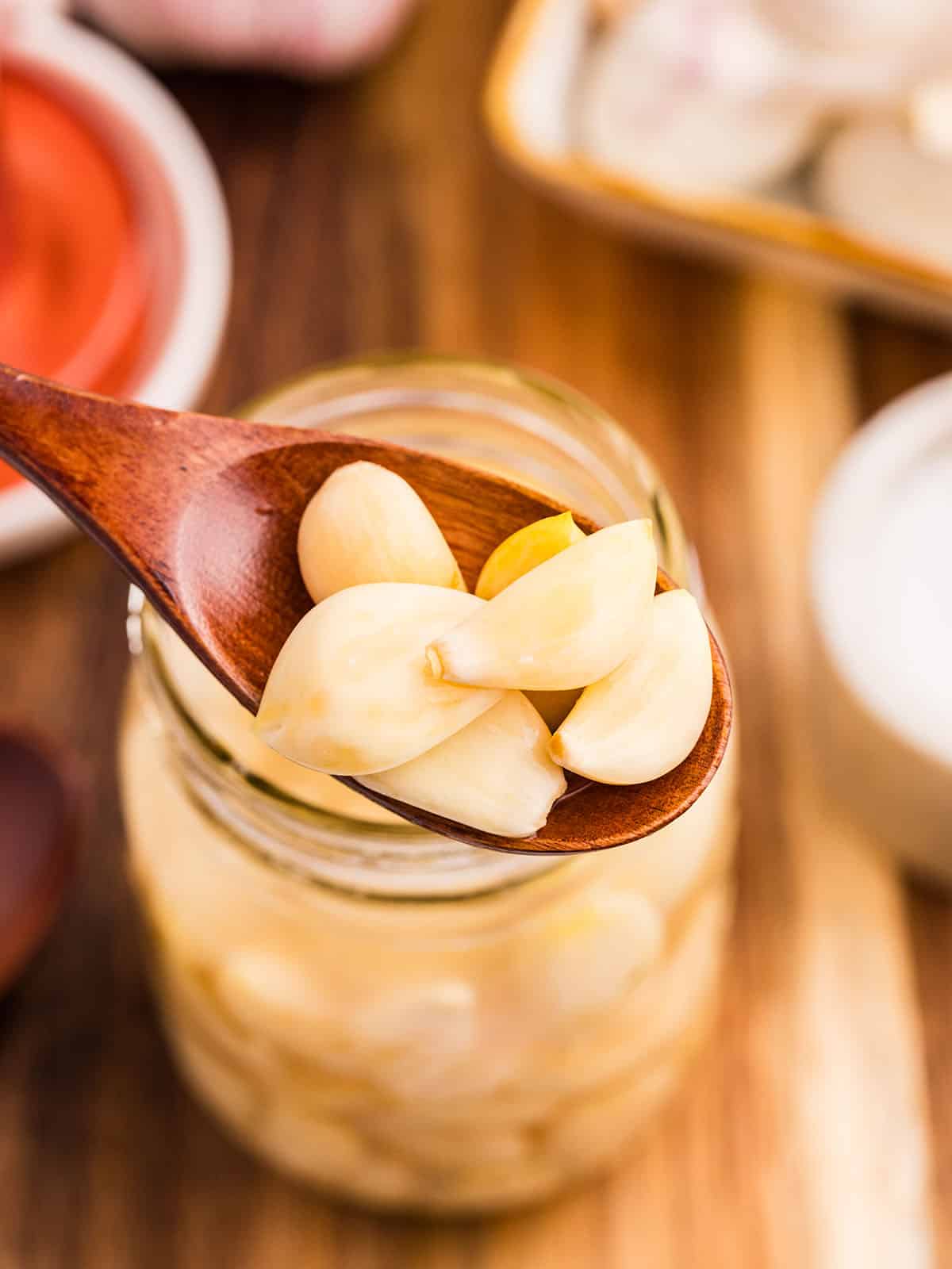 A wooden spoon lifting fermented garlic out of the jar, close to the camera. 