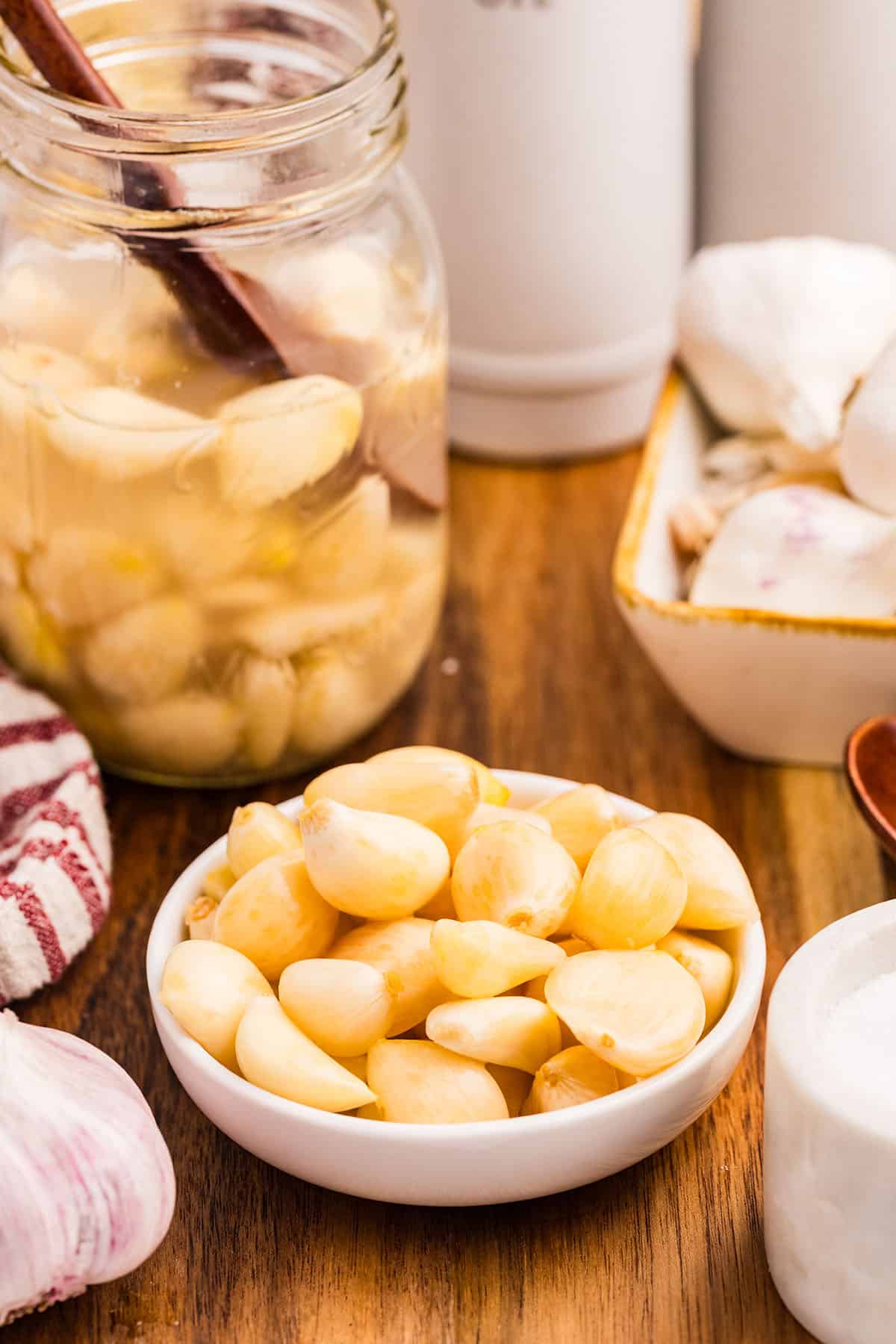 A bowl of fermented garlic on a wood surface with a jar of it in the background. 