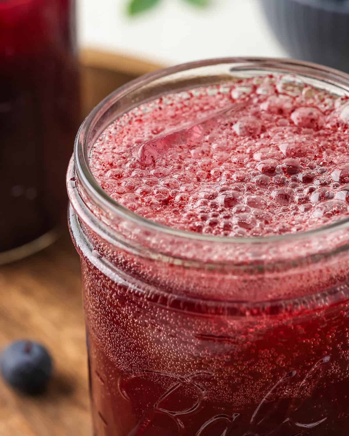 A jar of fizzy blueberry kombucha with bubbles on top, close up. 