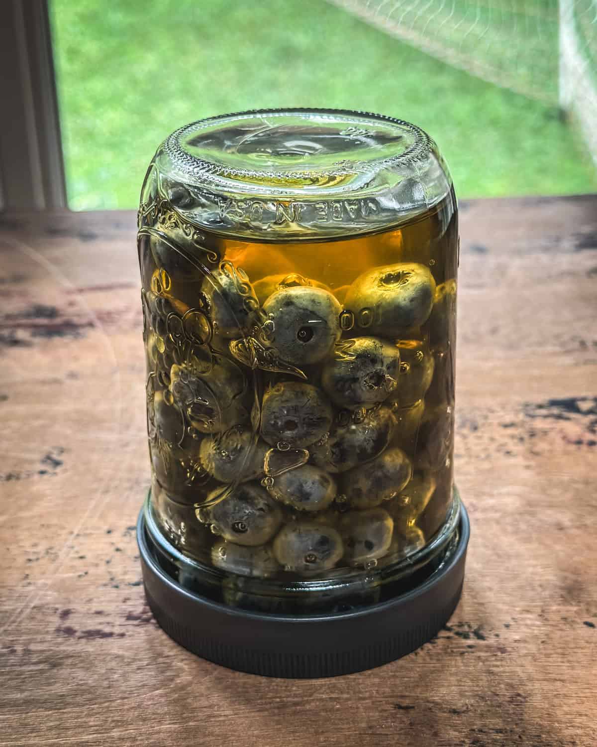 A jar of blueberries and honey with a lid upside down on a wood surface. 