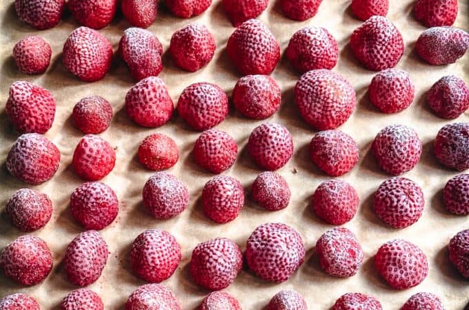 A baking sheet of frozen strawberries on parchment paper.