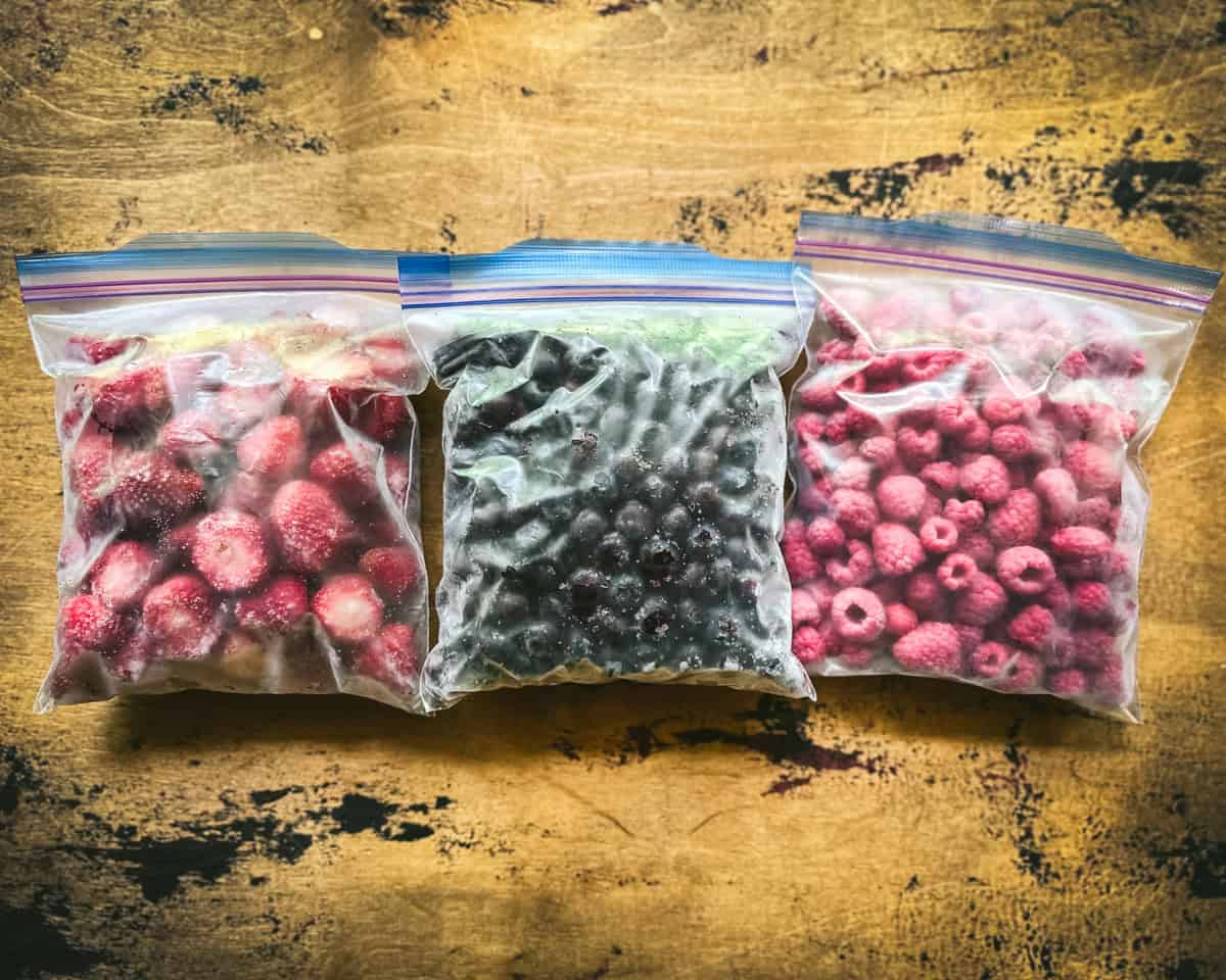 3 freezer bags of berries on a wood surface. 