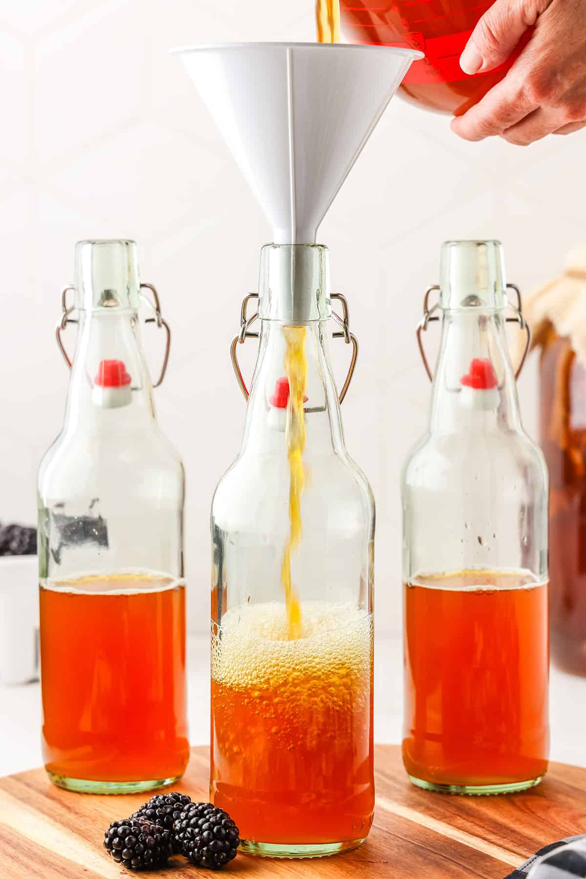 3 flip top bottles halfway filled with kombucha starter, one with a funnel on top with kombucha being poured in.