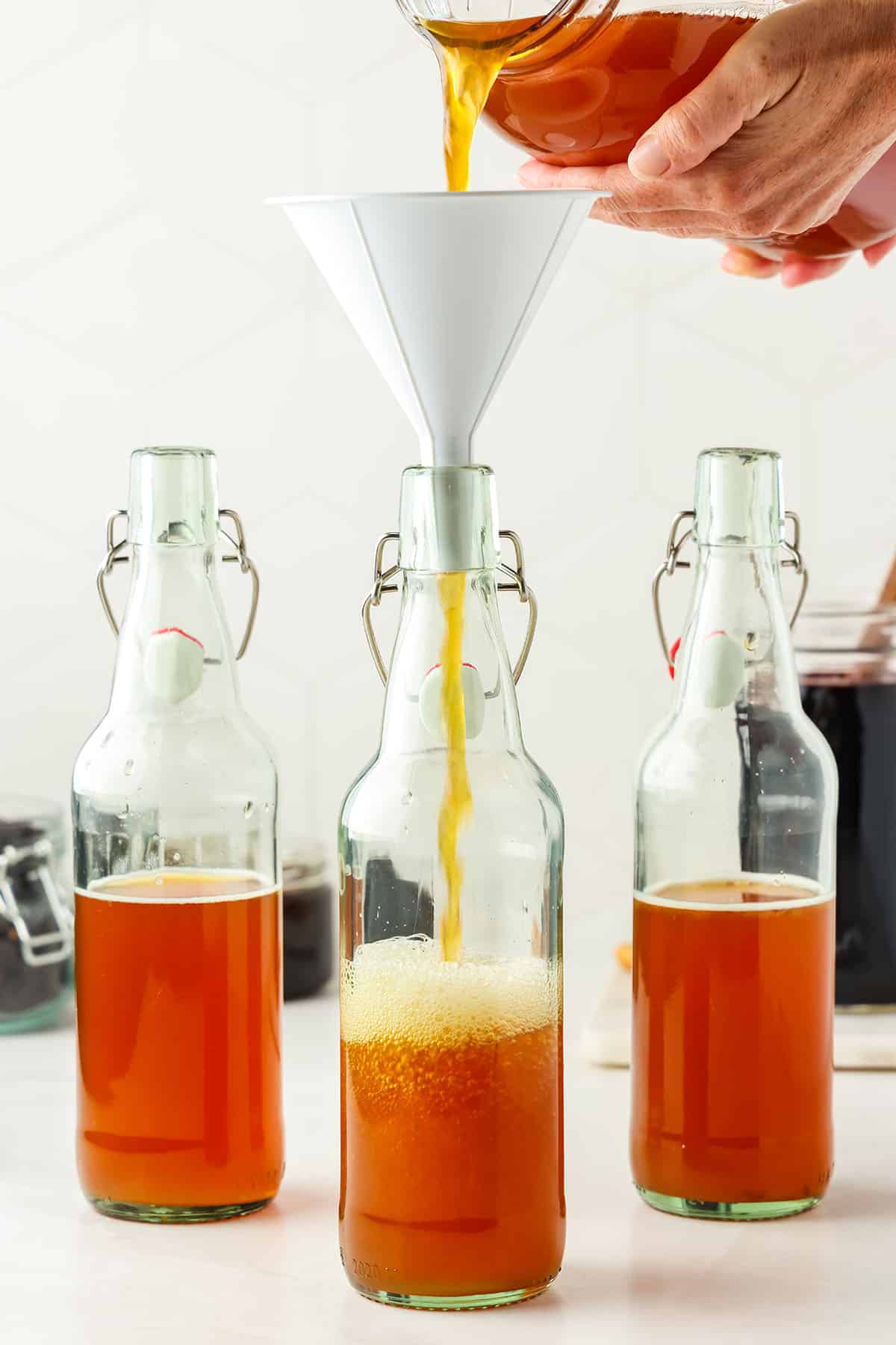 Kombucha being poured into bottles to fill them about halfway. 