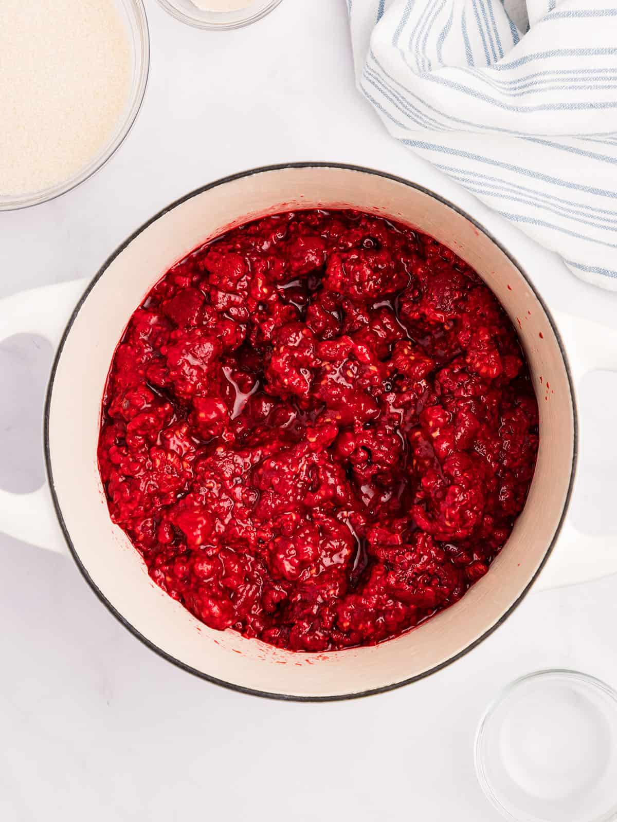 Mashed raspberries in a bowl on a white counter, top view. 