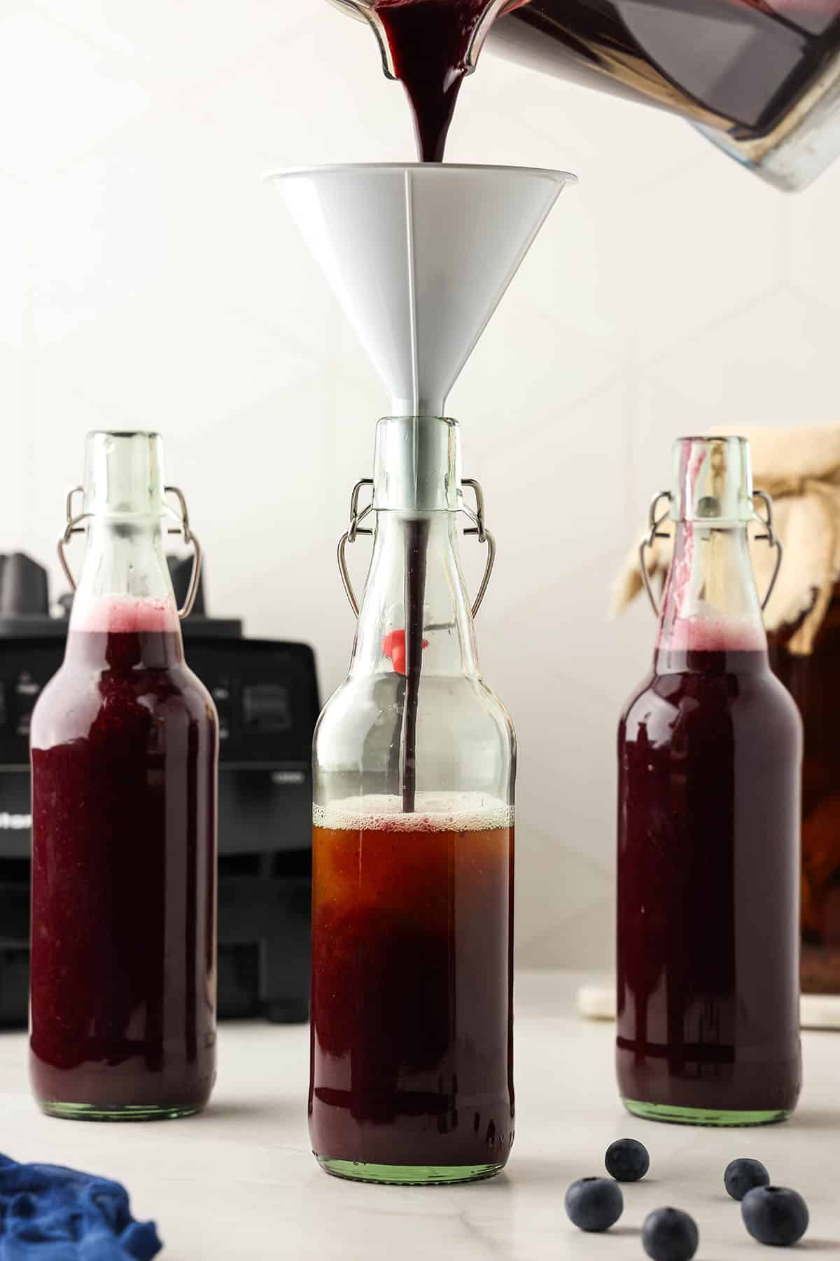 Flip top bottles with blueberry puree filling them up to the top over kombucha, surrounded by fresh blueberries. 