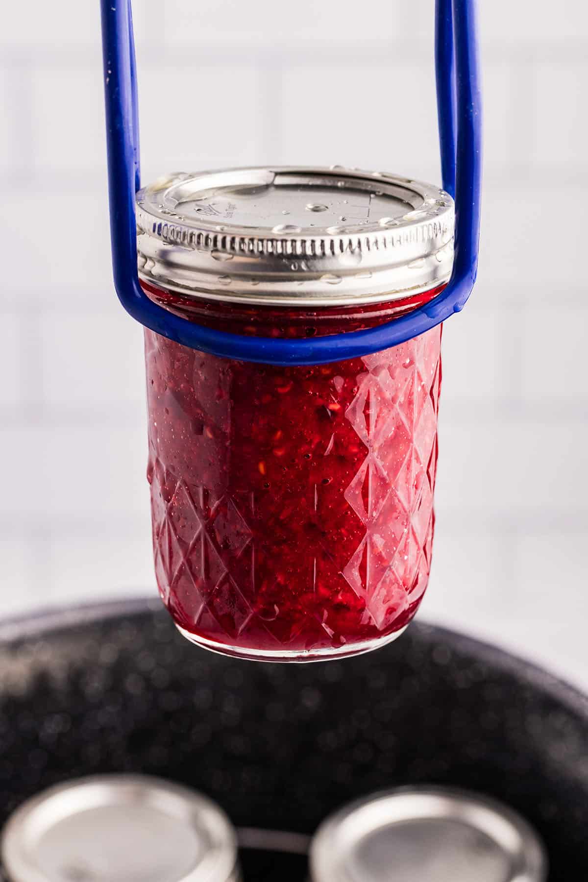 Raspberry jam being lifted from a water bath canning process with a jar lifter. 