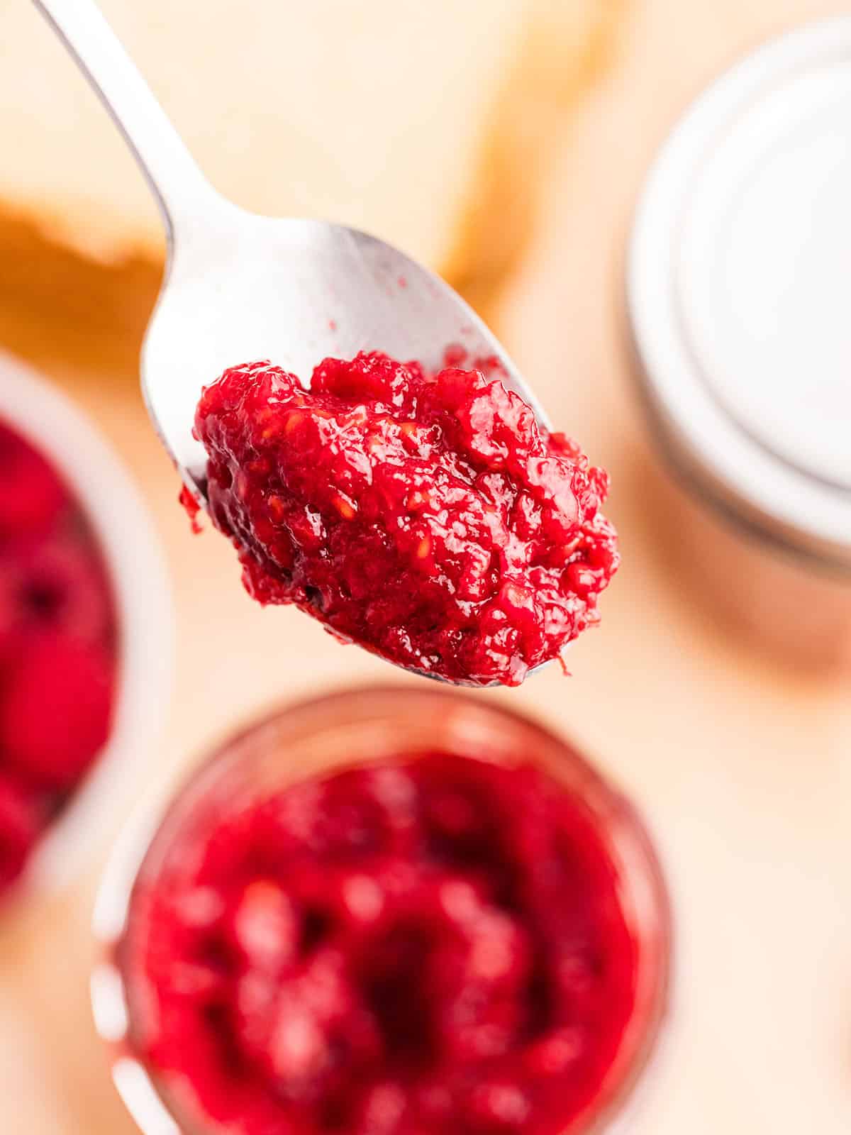 A spoonful of raspberry jam lifting up from a jar. 