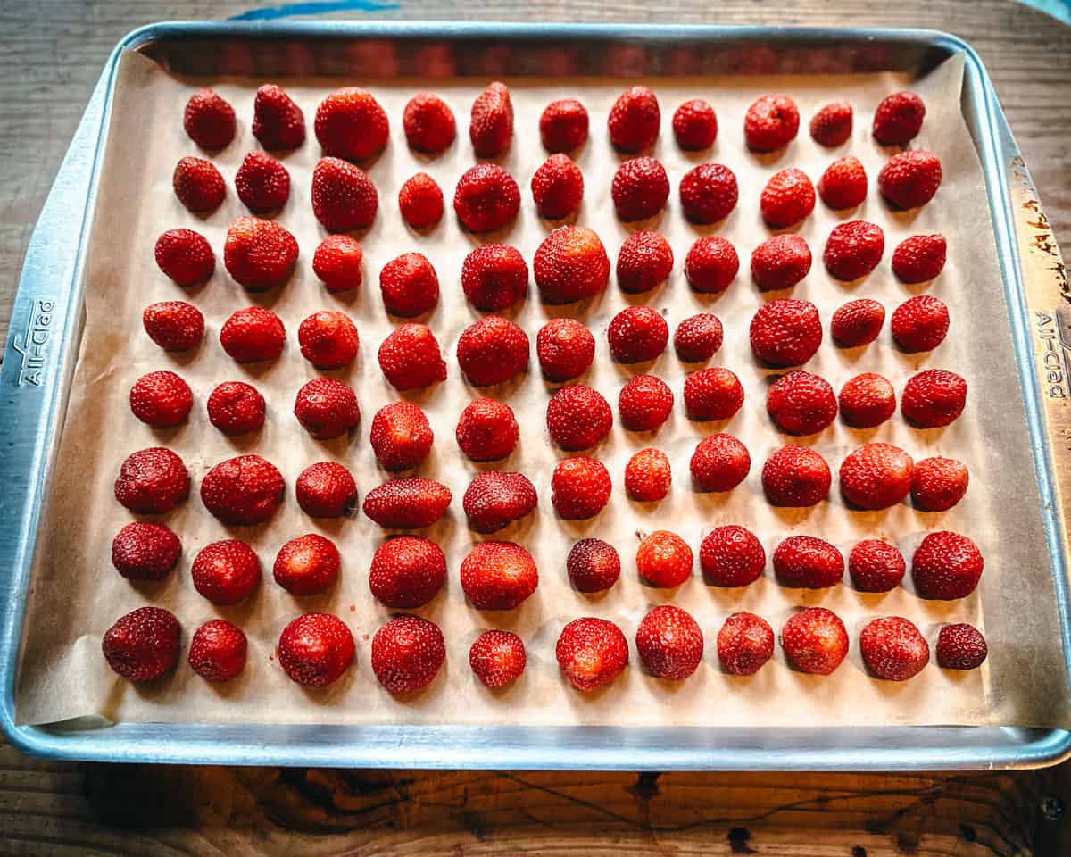 Strawberries on a sheet pan with parchment paper liner, with the stems cut off. 