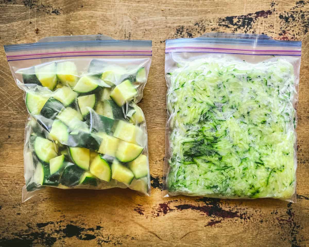 A bag of cubed and shredded frozen zucchini on a wood surface.