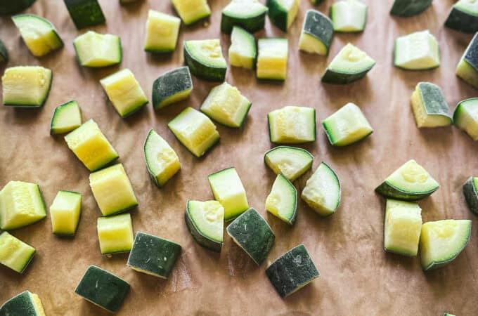 A baking sheet with frozen zucchini chunks on it.