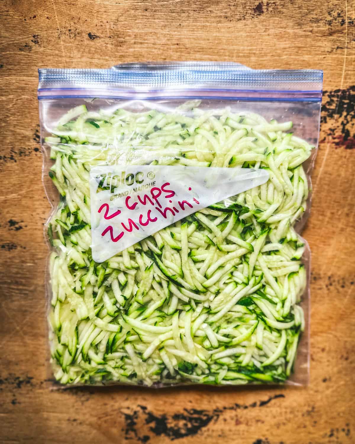 Shredded zucchini in a zip-top freezer bag on a wood surface. 