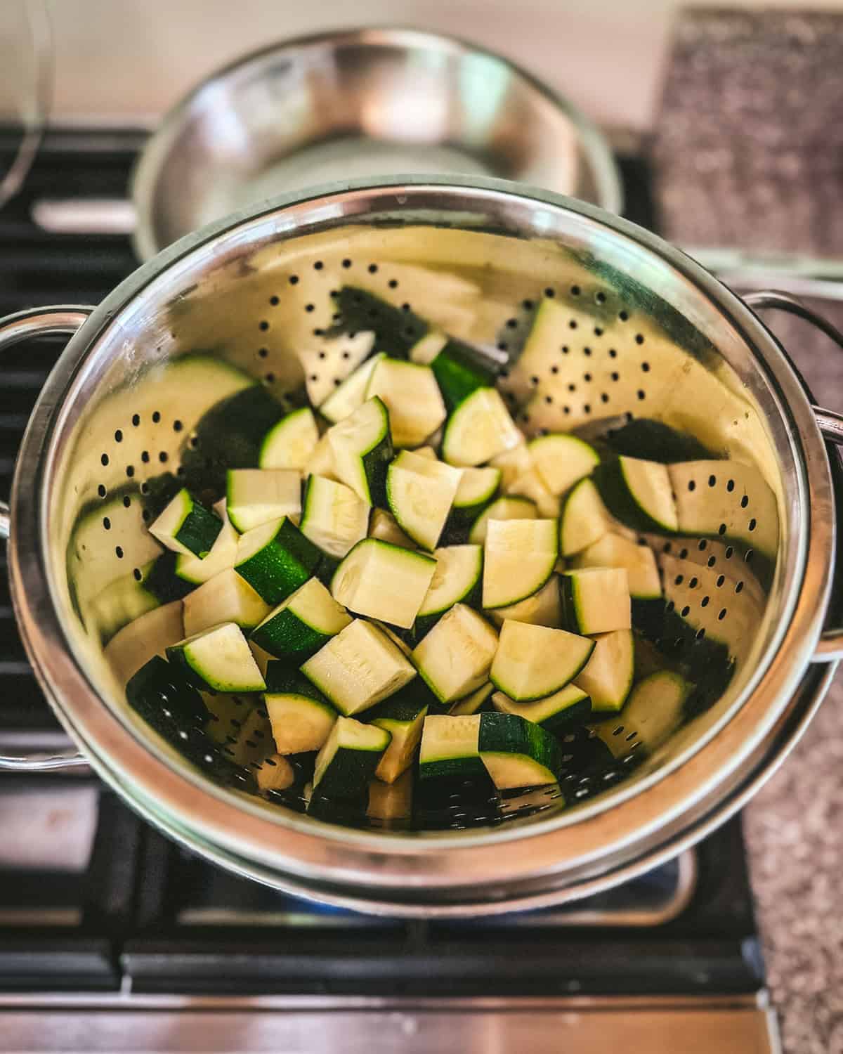 Zucchini chunks in a steamer basket on a stovetop. 