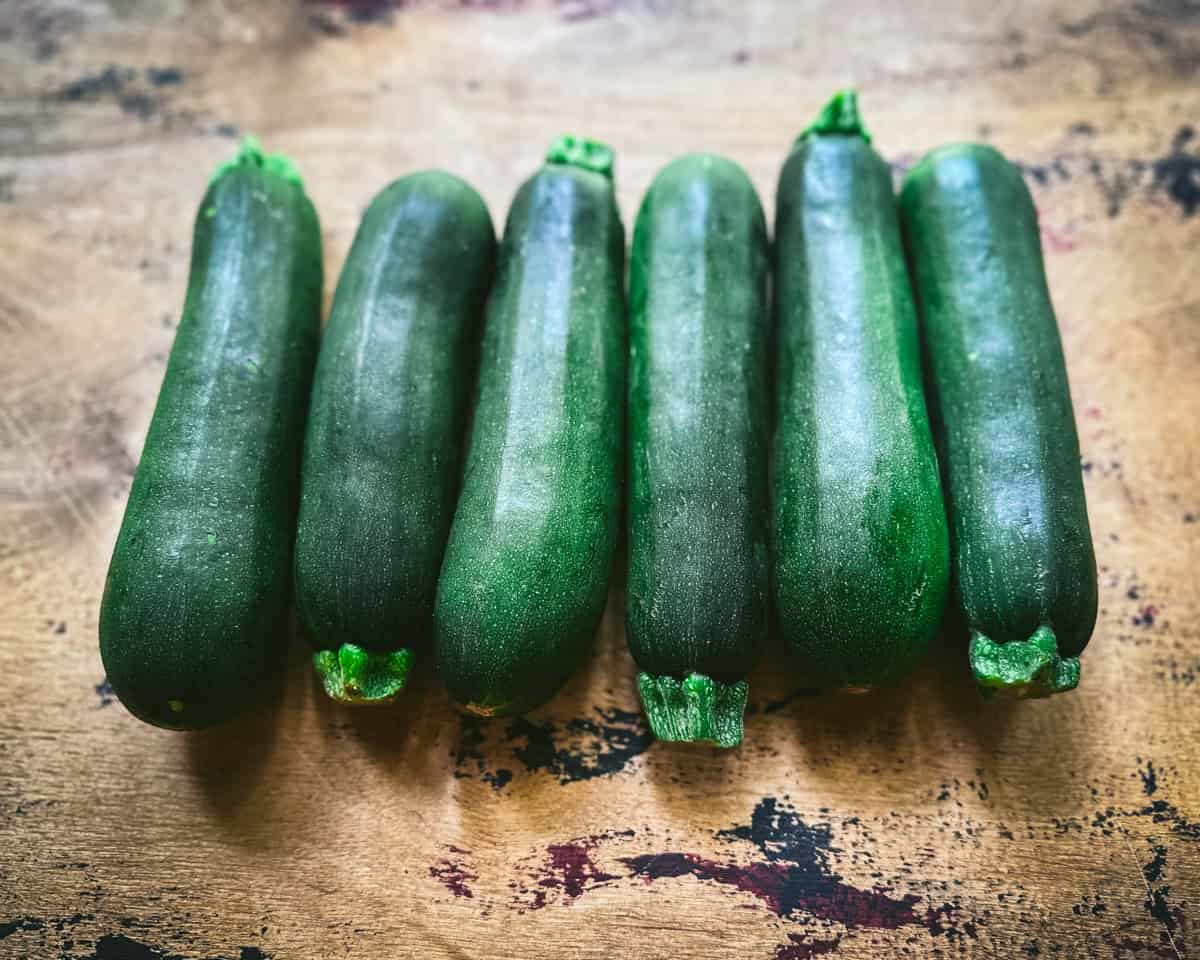 Fresh whole zucchinis lined up on a wood cutting board. 