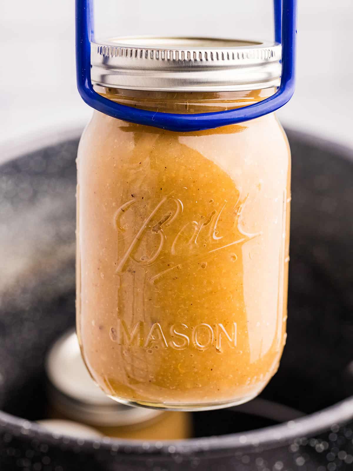 A jar of applesauce going into a water bath canner with a jar lifter. 