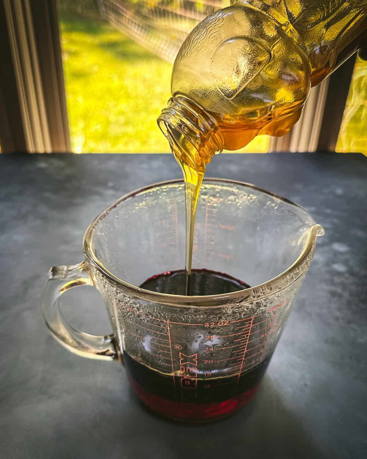 Honey pouring into a pyrex glass with aronia infused water in it. 