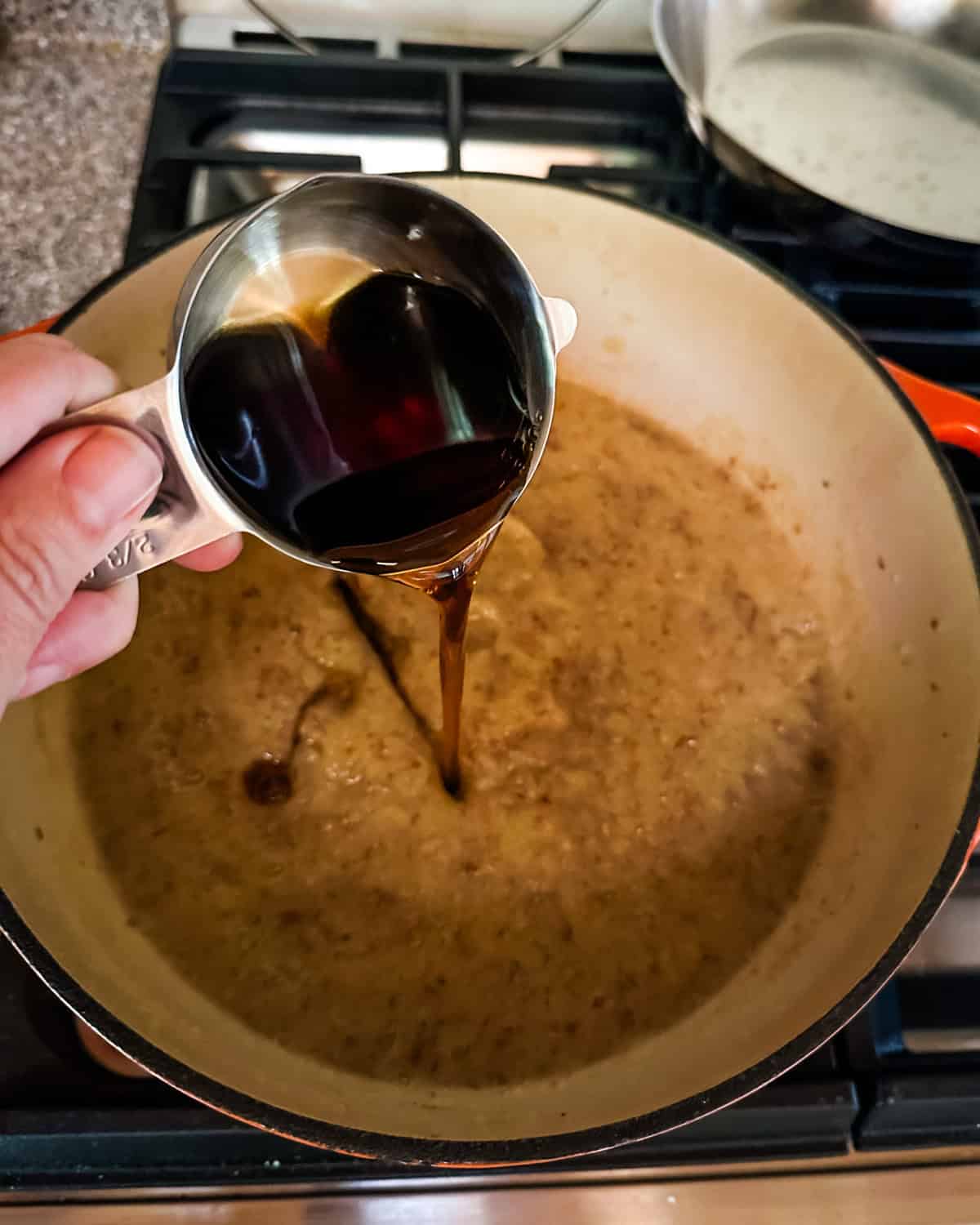 Maple syrup pouring from a measuring cup into the pot of pear puree.