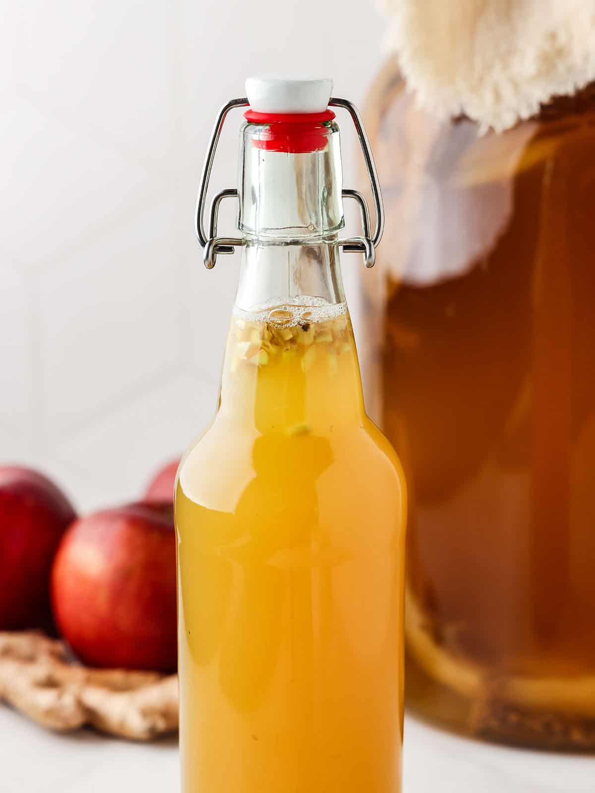 Apple ginger kombucha with bubbles at the top, surrounded by fresh apples and a gallon jar of plain kombucha. 