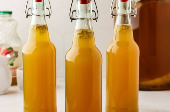 3 flip top bottles of apple ginger kombucha on a white counter.