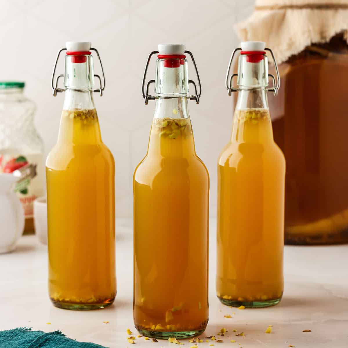 3 flip top bottles of apple ginger kombucha on a white counter. 